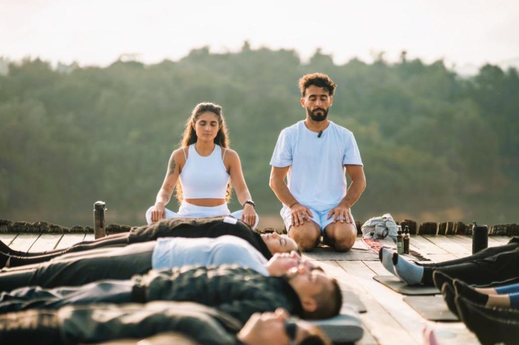 Un grup de persones meditant a l'aire lliure sobre un pont de fusta, amb un paisatge natural de fons.