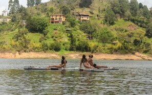 Un grup de persones en una balsa sobre aigües tranquil·les, amb cases a la base d'un turó al fons.