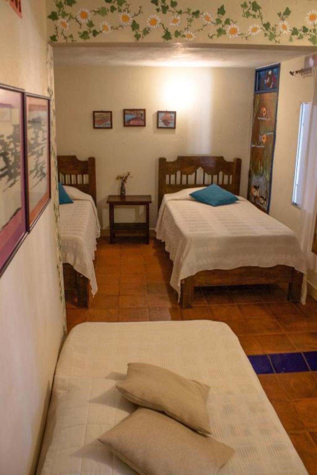 A room with two wooden beds, a small table, and a wall with framed pictures.