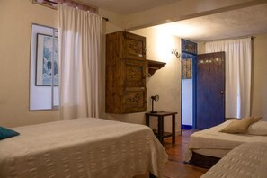 A room with two beds, a wooden cabinet, a small table, and a door leading to another room.