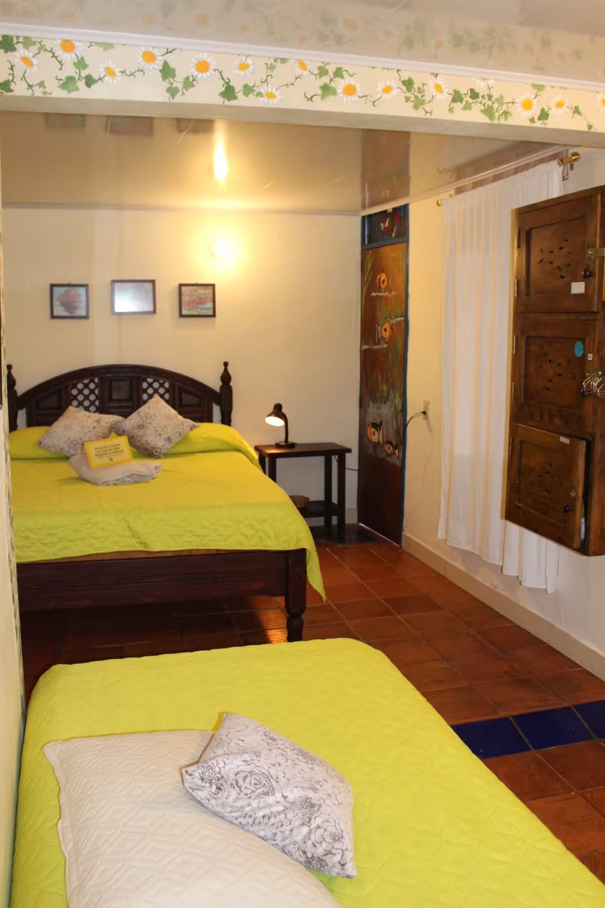 A hotel room with two beds, a nightstand, a wall-mounted painting, and a wooden door.