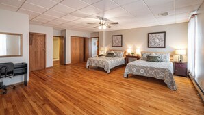 Ein Hotelzimmer mit zwei Betten, einem Schreibtisch, einem Stuhl und einem Deckenventilator.