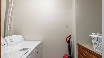 A laundry room with a washing machine, a vacuum cleaner, and a wooden cabinet.