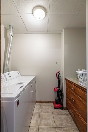 A laundry room with a washing machine, a vacuum cleaner, and a wooden cabinet. - Stay and Play Downtown La Crosse Apartment! (La Crosse)