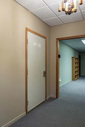 A hallway with a door labeled 'APT 301' and a wooden bookshelf. - Stay and Play Downtown La Crosse Apartment! (La Crosse)