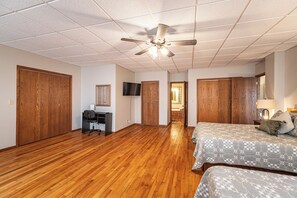 Une chambre avec un plancher en bois, un ventilateur de plafond, un bureau avec une chaise et un lit avec une literie à motifs.