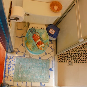 A bathroom with a mosaic floor, a toilet with a fish decoration, a roll of toilet paper, and a trash bin. - Tulipan - Single suite with lake view (Guatapé)