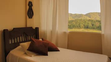A bed with a headboard, a window with curtains, and a view of a mountainous landscape.