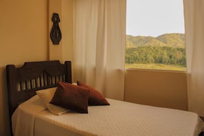 A bed with a headboard, a window with curtains, and a view of a mountainous landscape.