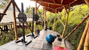 Área de ginástica ao ar livre com equipamentos de exercícios, uma bola de exercício azul e um tapete vermelho.
