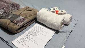 Un letto con testiera in legno, biancheria grigia e un set di asciugamani e una brochure sul letto.