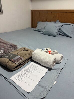A bed with a wooden headboard, grey bedding, and a set of towels and a brochure on the bed. - Comfort & Convenience | 2-Bedroom Apartment - Wi-Fi and Parking (Cotia)