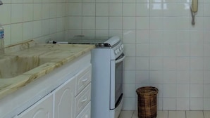 Una cucina con piastrelle bianche, un fornello, un lavandino e un cestino.