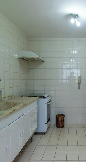 A kitchen with white tiles, a stove, a sink, and a trash bin. - Comfort & Convenience | 2-Bedroom Apartment - Wi-Fi and Parking (Cotia)