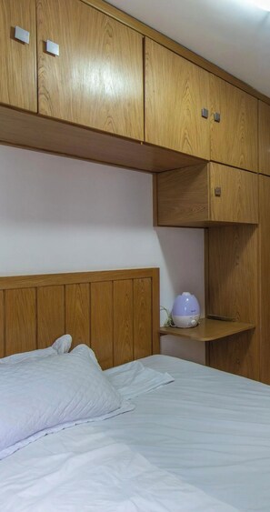 Een slaapkamer met een bed, een houten garderobe en een nachtkastje met een lamp.