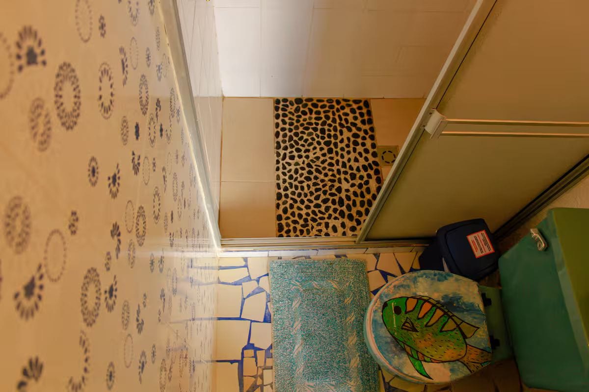Quarto com papel de parede estampado, uma parede de destaque com estampa de leopardo, uma lixeira verde e uma mala azul.