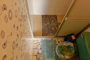 A room with patterned wallpaper, a leopard print accent wall, a green trash bin, and a blue suitcase.