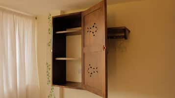 A room with a wooden cabinet with a hinged door, a small shelf, and a hook for hanging items.