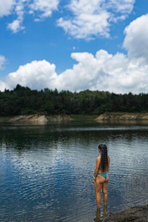 A person standing by a calm body of water with a forested landscape in the background.