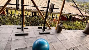 Área de ginástica ao ar livre com equipamentos de exercício, incluindo barra, anilhas e uma bola de ginástica azul.