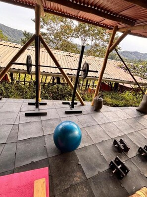 Ein Outdoor-Fitnessbereich mit Trainingsgeräten, darunter eine Langhantel, Gewichte und ein blauer Trainingsball.