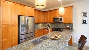 A kitchen with wooden cabinets, stainless steel appliances, granite countertops, and pendant lighting. - Mauna Lani Fairways Resort Townhouse w/ Beach Club (Waimea)