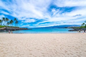 Uma praia com águas azul-claras, palmeiras e um trecho de costa rochosa.