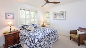 A bedroom with a bed, a chair, a nightstand, a lamp, a ceiling fan, and two windows with blinds. - Mauna Lani Fairways Resort Townhouse w/ Beach Club (Waimea)