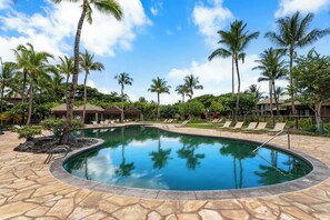 Ein Pool mit Liegestühlen und Palmen, umgeben von Gebäuden und Grünpflanzen.