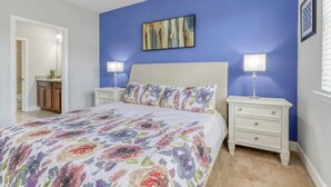 Quarto com cama, duas mesas de cabeceira com luminárias, um quadro na parede e porta para outro cômodo.