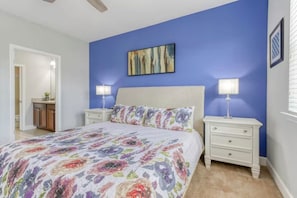 Un dormitorio con cama, dos mesitas de noche con lámparas, un cuadro en la pared y una puerta que da a otra habitación.