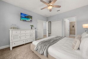 Ein Schlafzimmer mit einem Bett, einem Schminktisch, einem Deckenventilator und einem Bild an der Wand.
