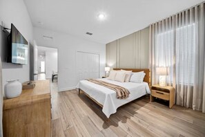 Ein modernes Schlafzimmer mit einem großen Bett, Nachttischen, einem Flachbildfernseher und Holzboden.