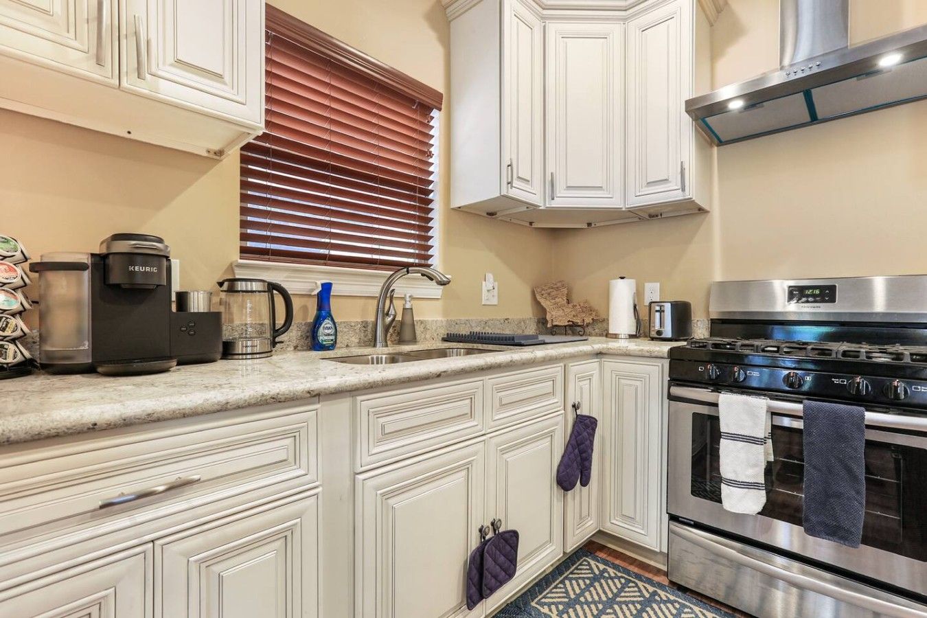 A kitchen with white cabinetry, a stainless steel range, a coffee maker, and a window with blinds.