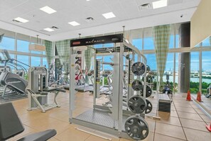 A gym with various exercise equipment, including treadmills and weightlifting stations, with a view of a cityscape through large windows. - Luxury 2-bedroom apartment with amenities in Downtown Miami, featuring ocean and park views (Miami)