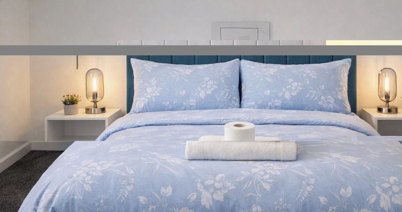 Ein ordentlich gemachtes Bett mit Blumenmuster, zwei Nachttische mit Lampen und einer Wandleuchte.