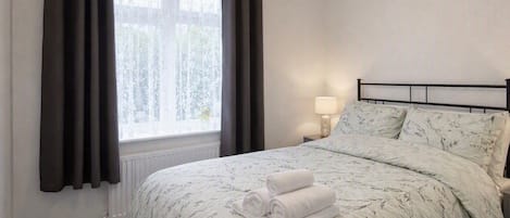 A bedroom with a bed, a window with curtains, a bedside lamp, and a radiator.