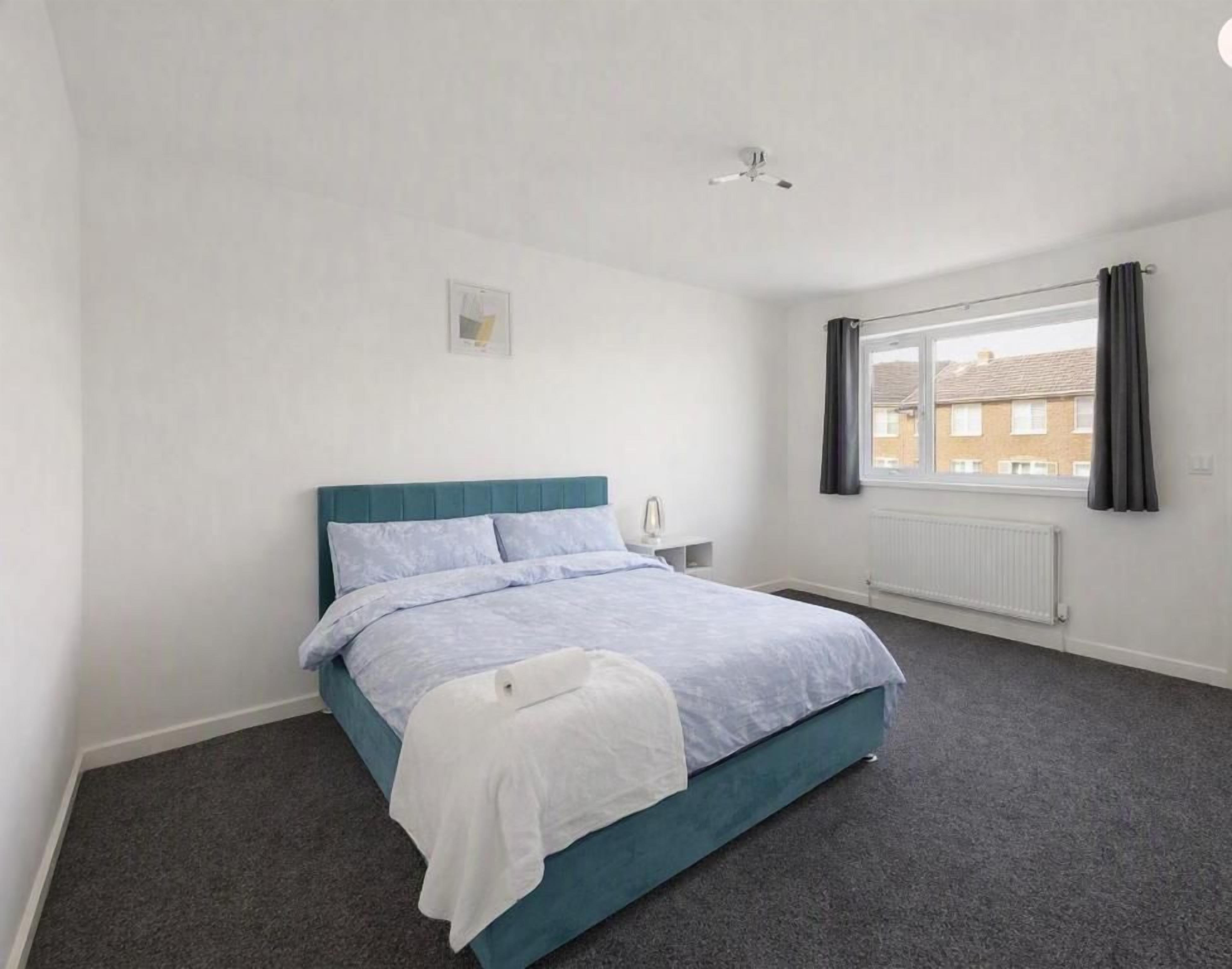 Un dormitorio con cama, ventana con cortinas, radiador y ventilador de techo.