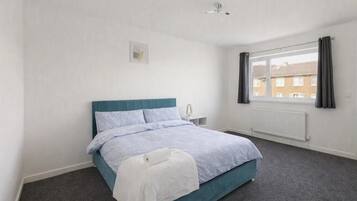 A bedroom with a bed, a window with curtains, a radiator, and a ceiling fan.