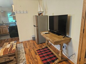 A compact kitchen with a refrigerator, a wooden dining table, and a television on a stand.