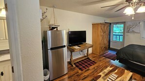Espaço compacto para viver, com cozinha compacta, televisão, ventoinha no teto e um armário de madeira.