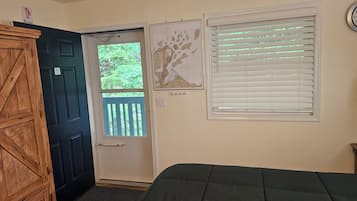 A room with a door, a window with blinds, a bed, and a wall-mounted clock.