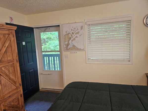 A room with a door, a window with blinds, a bed, and a wall-mounted clock.