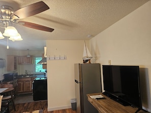 A kitchen with wooden cabinets, a refrigerator, a wooden dining table, and a ceiling fan.