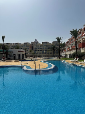 Ein Pool mit geschwungener Kante, umgeben von Liegestühlen und Palmen.