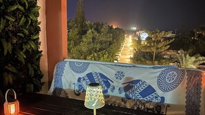 Ein Balkon mit Tisch, zwei Laternen und Blick auf eine beleuchtete Stadt bei Nacht.