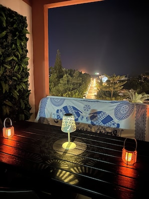 Ein Balkon mit Tisch, zwei Laternen und Blick auf eine beleuchtete Stadt bei Nacht.