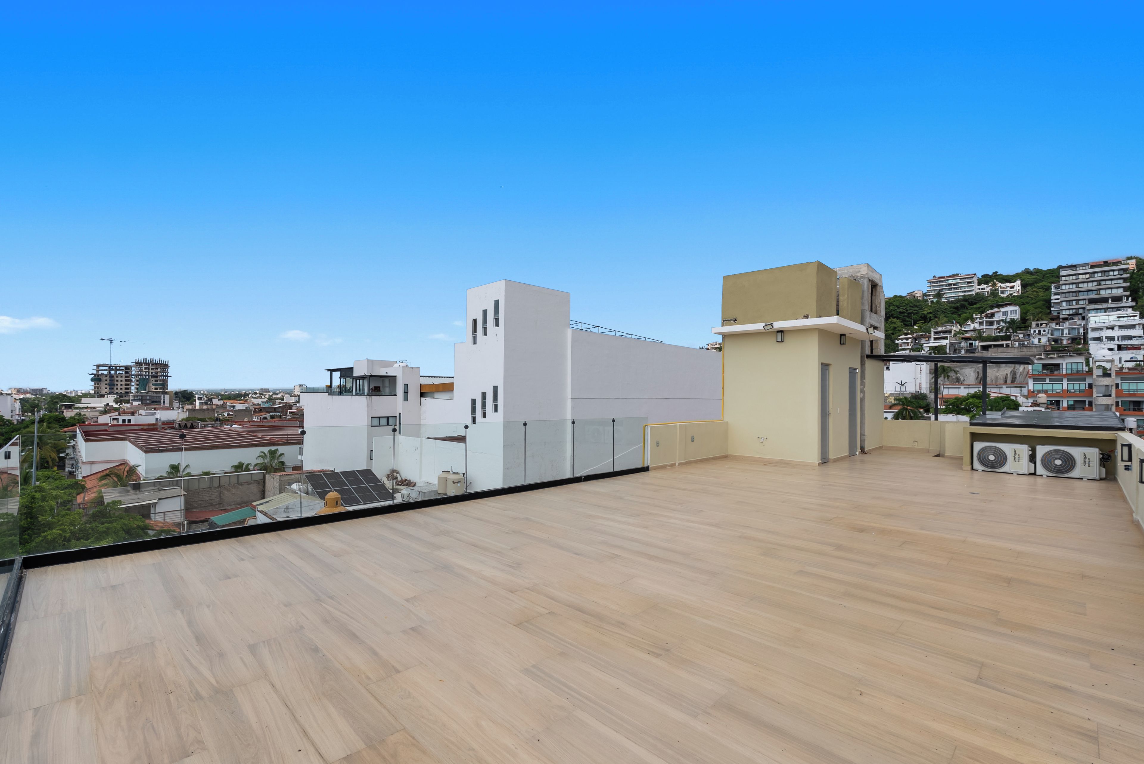 Une terrasse sur le toit offrant une vue dégagée sur le paysage urbain, avec des bâtiments modernes et une colline visible au loin.
