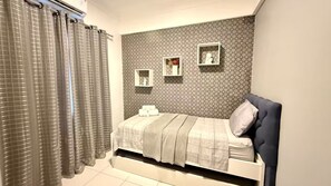 Un dormitorio con cama, cortinas, cabecero y estantes empotrados con objetos decorativos.