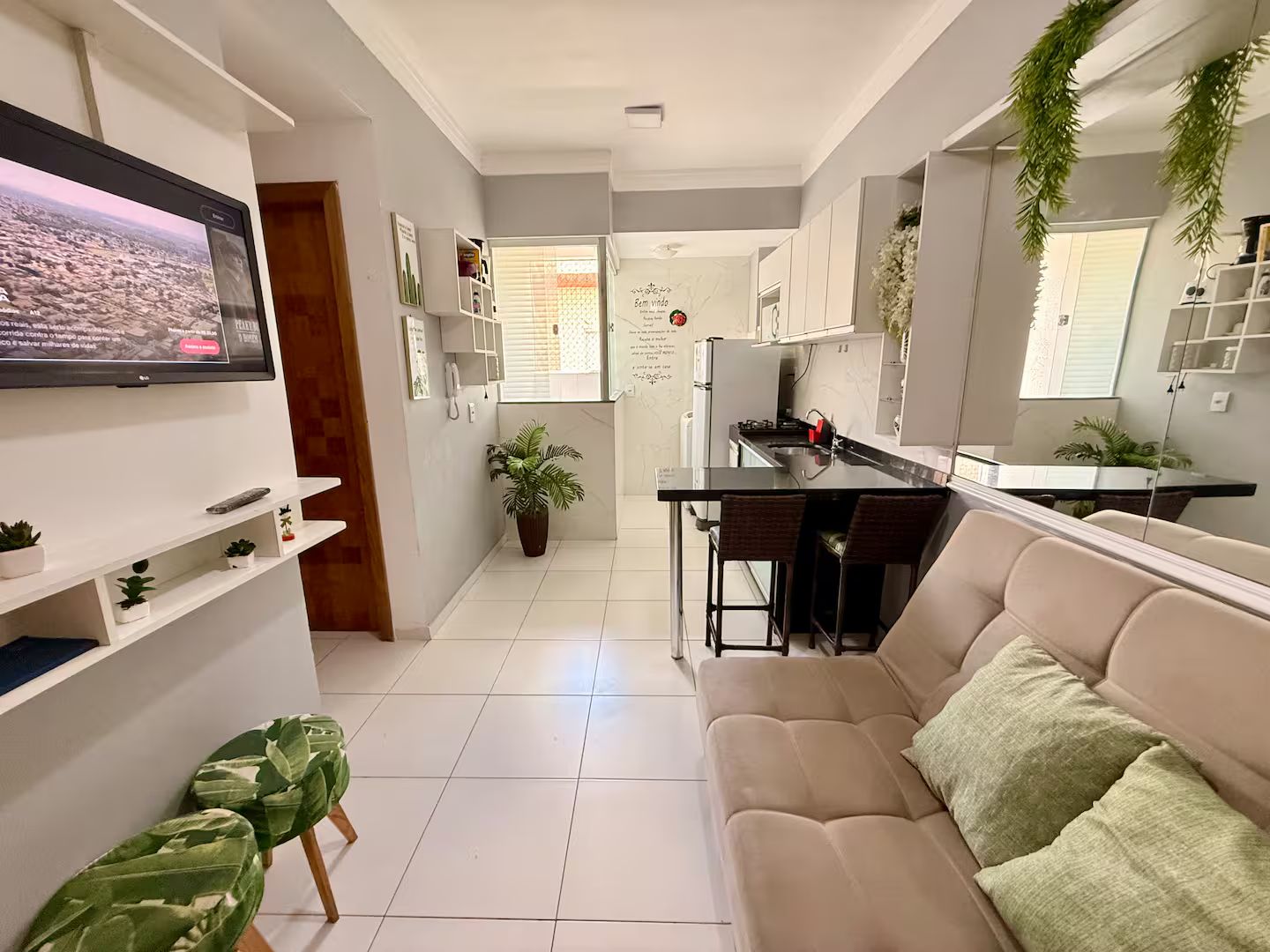 Uma sala de estar moderna com televisão de tela plana, um sofá e um espaço de jantar com cozinha ao fundo.